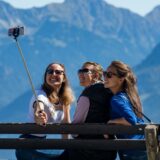 Drei Frauen sitzen auf einer Bank in den Bergen und machen ein Selfie.