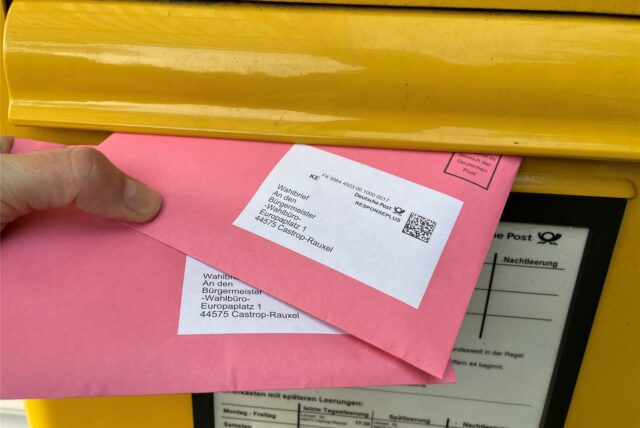 Ein Briefkasten, in den jemand Briefwahlumschläge legt.