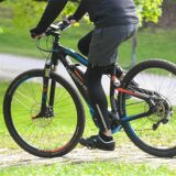 Ein Mann fährt mit einem E-Bike der Marke Haibike durch einen Park. Das Fahrrad hat eine schwarze Lackierung mit blauen und roten Akzenten.