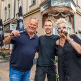 Elke Moschny und Dirk Lasarz alias Duo Just4Fun stehen mit einem Mikrofon in der Hand in der Innenstadt von Herten. Tontechniker Robin Pospiech steht zwischen ihnen.