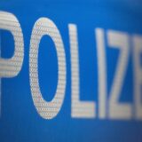 Nahaufnahme der teilweise unscharfen Aufschrift „POLIZEI“ in weiß auf blauem Grund. Die Buchstaben weisen eine reflektierende Wabenstruktur auf.