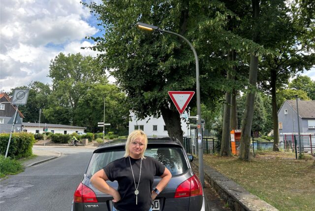 Frau vor einem Auto und einer brennenden Laterne, ist empört