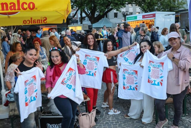 Mehrere Besucherinnen halten T-Shirts der Band „Furumba“ in die Kamera.