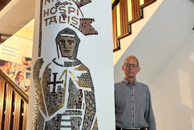 Deltef Herbers steht im Haupthaus der Kommende Dortmund neben einem Mosaik eines Ritter des Deutschen Ordens.