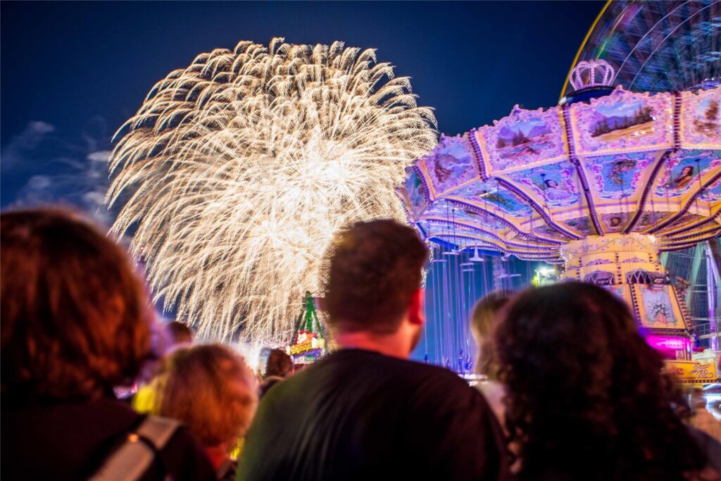 Gäste der Cranger Kirmes verfolgen das Kirmes-Feuerwerk am Himmel.