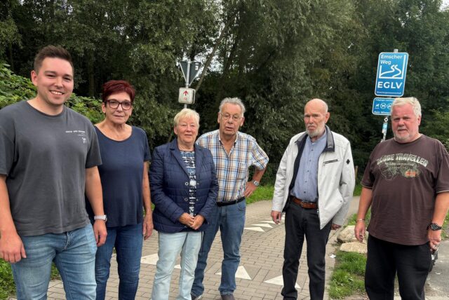 Eine Gruppe von sechs Personen steht vor einem Schild des Emscher Weges. Die Personen sind unterschiedlichen Alters und tragen Freizeitkleidung.