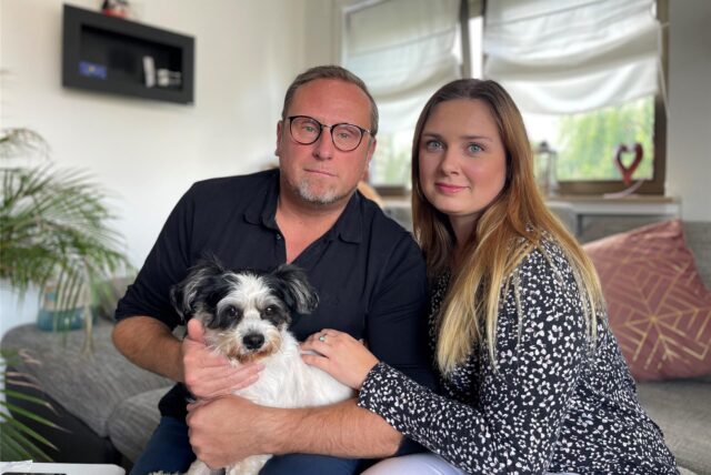 Christian und Madlaine Laske sitzen mit ihrem Hund Lucky auf ihrer Couch im Wohnzimmer, in dem vor einigen Tagen die Polizei stand. Das Ehepaar ist Opfer von „Swatting“ geworden.