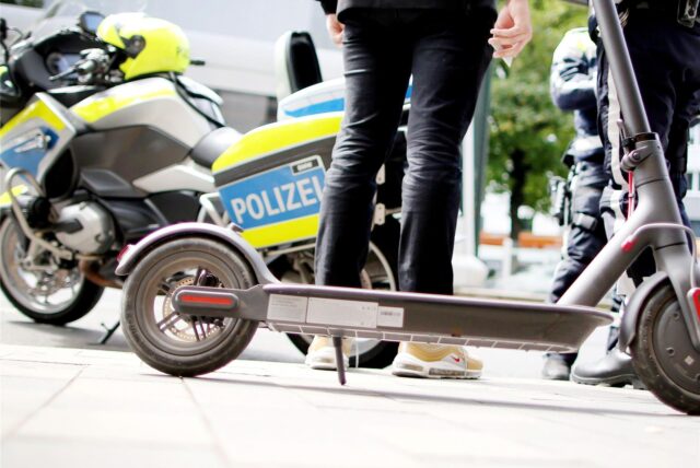 E-Scooter und Polizeimotorrad am Straßenrand in der Stadt.