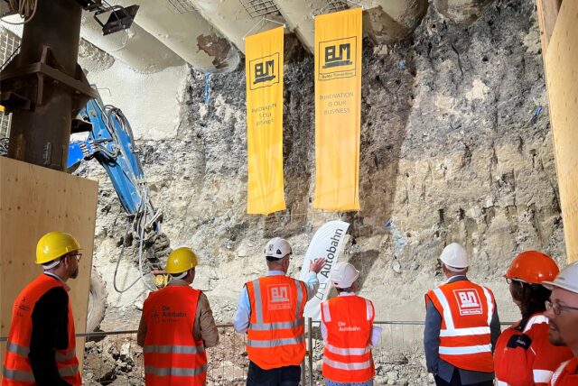 Sieben Menschen in Warnwesten und mit Helmen auf dem Kopf stehen auf einer Baustelle vor einer Wand aus Gestein. Das Foto ist unmittelbar vor dem Durchstich des neuen Tunnels unter dem Kreuz Herne entstanden.
