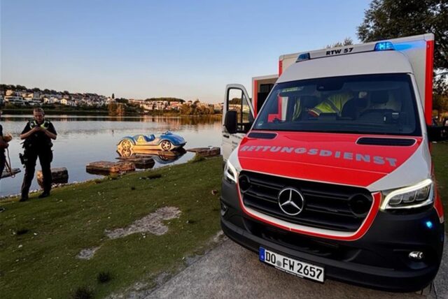Ein Rettungswagen steht am Ufer des Phoenix-Sees. Im Hintergrund spiegelt sich die Landschaft auf der Wasseroberfläche. Ein Tretboot schwimmt am Ufer.