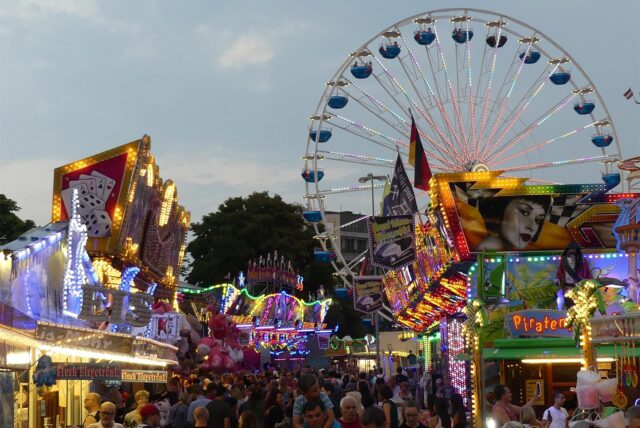Das Riesenrad und einige Spielbuden erstrahlen in bunten Farben in der Dämmerung.