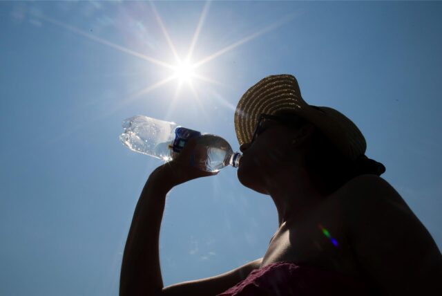 Eine Frau mit Sonnenhut trinkt am 03.07.2015 in Recklinghausen (Nordrhein-Westfalen) unter der Mittagssonne aus einer Wasserflasche.