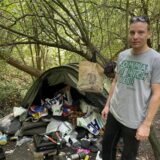 Ein Mann steht vor einem zugemüllten Zelt in einem Wald in Dortmund.
