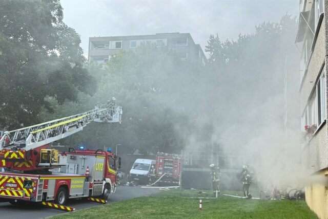 Drehleiterwagen und Feuerwehrleute vor einem Wohnhaus im Adelhardweg in Nette. Aus den Kellerfenster dringt dichter Rauch.
