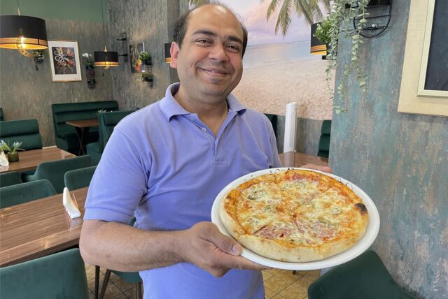 Gastronom Muhammad Irfan steht in seinem Lokal in Lütgendortmund und hält eine Pizza-Teller in der Hand.