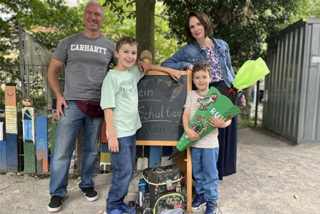 Rudi (vorne Rechts), sein Bruder Felix (vorne Links) und die Eltern posieren für ein Einschulungsfoto auf dem Schulhof der Franziskusschule im Kaiserviertel.