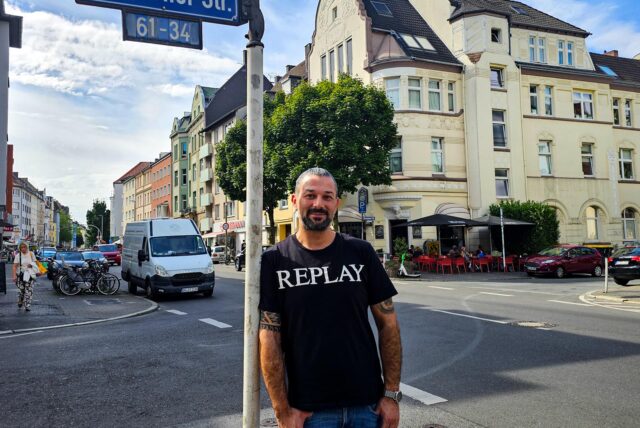 Friseur Ufuk Demirel lehnt an einem Straßenschild an der Saarlandstraße in Dortmund.
