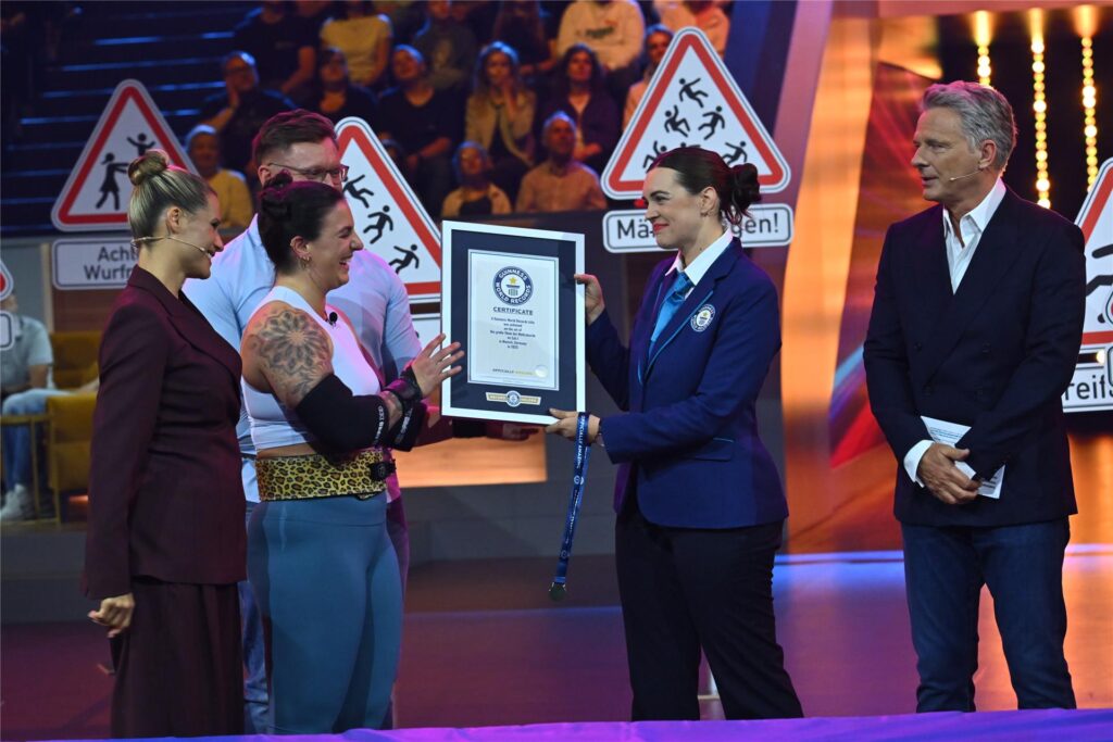 Die Dortmunder Sina Ruppenthal bekommt in der Sat1 Live-Show „Guinness World Records – Die große Show der Weltrekorde“ eine Urkunde überreicht. Die Moderatoren Michelle Hunziker und Jörg Pilawa stehen daneben.