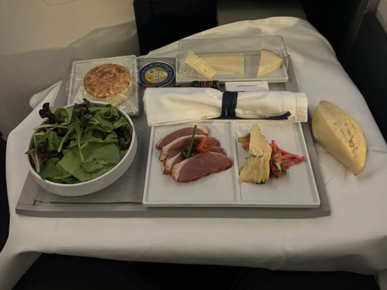 Tablett mit Essen, bestehend aus Salat, Käsekuchen, Brot und anderen Speisen, auf einem Tablett im Flugzeug.
