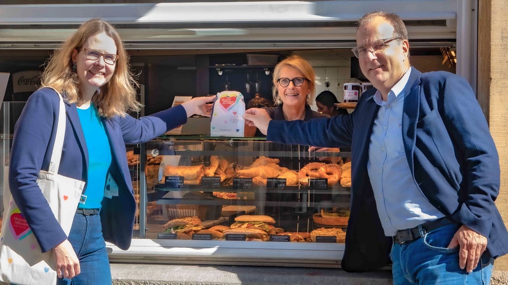 Pia Stapel (Caritasverband für die Diözese Münster e.V., links) und Georg Krimphove nehmen die Brötchentüten in der Filiale „pain et gâteau“ am Michaelisplatz in Münster entgegen.