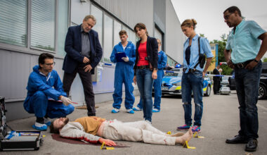 "SOKO München - 24 Stunden": Am Tatort auf einem grauen Industriegelände liegt eine Leiche auf dem Boden. Um diese herum steht das SOKO-Team bestehend aus Arthur Bauer (Gerd Silberbauer), Katharina Hahn (Bianca Hein), Toni Bischoff (Amanda da Gloria) und Franz Ainfachnur (Christofer v. Beau) und schauen sich die Leiche näher an. Dr. Weissenböck (Florian Odendahl) sitzt in der Hocke am Kopf der Leiche, er hält einen Stift in der Hand. Im Hintergrund sind zwei Mitarbeiter der Spusi (Komparsen) und ein Polizeiauto zu sehen.