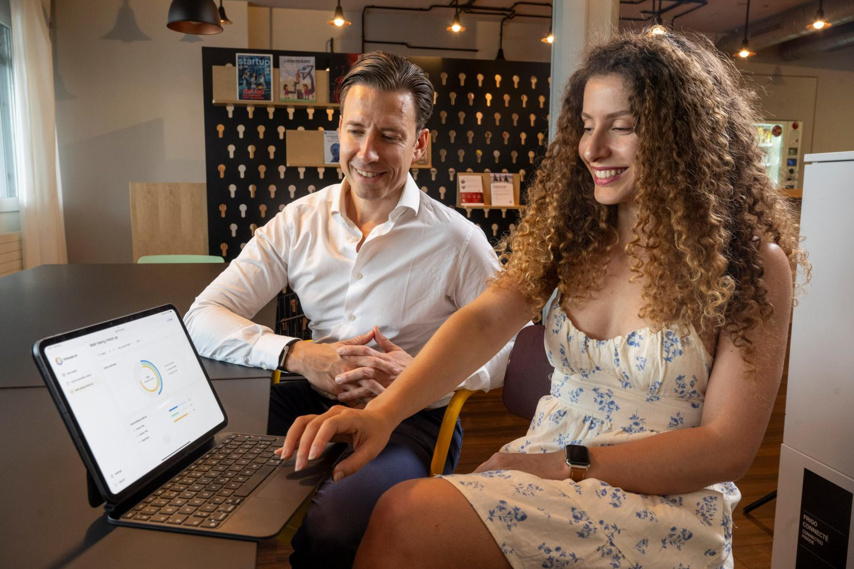 Ein Mann und eine Frau, die circa 35 Jahre alt sind, sitzen an einem Tisch und schauen auf einen Laptop-Bildschirm, der eine Diagramm-Analyse zeigt.