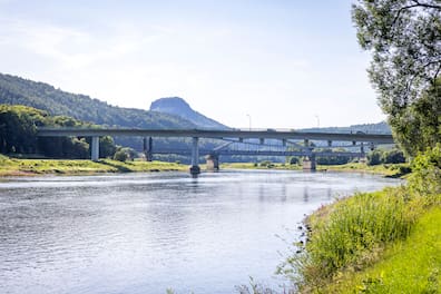 Die Elbbrücke in Bad Schandau (im Vordergrund). Diese war monatelang gesperrt und kann seit April wieder befahren werden, allerdings nur von Fahrzeugen, die nicht schwerer sind als 7,5 Tonnen (mit Ladung). Das Brückenbauwerk dahinter ist eine Bahnbrücke, die auch Carolabrücke heißt wie die eingestürzte und aktuell nicht mehr vorhandene Brücke in Dresden. Allerdings ist die 1877 eröffnete Bad Schandauer Carolabrücke kein Spannbetonbau.