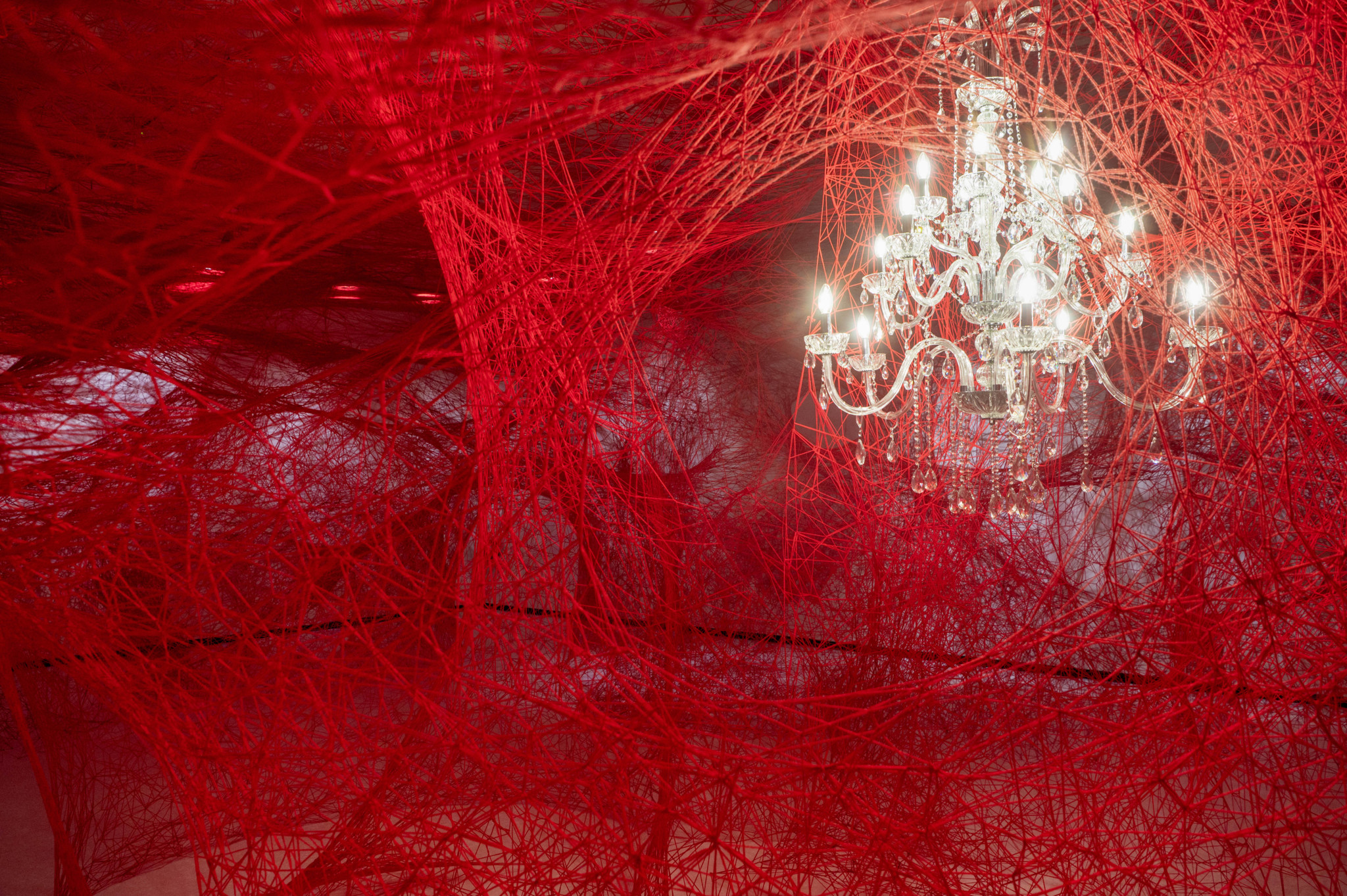Kunstinstallation von Chiharu Shiota mit rotem Garn und Kronleuchter im Kunst- und Geschichtsmuseum Fribourg.
