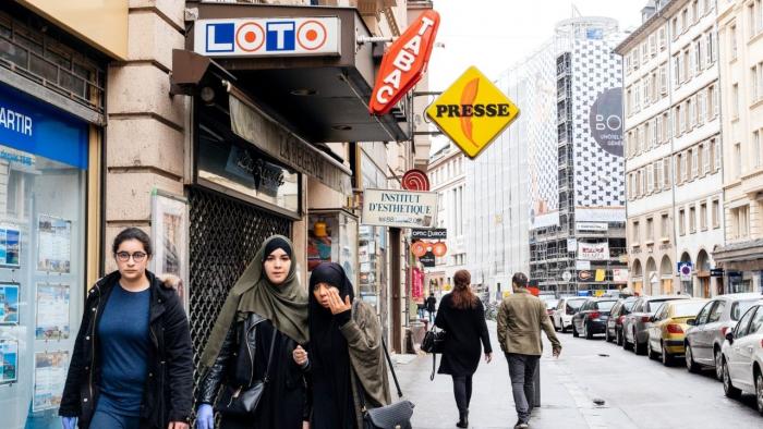 Drei muslimische Mädchen gehen auf dem Trottoir unter Loto- und Presseschildern in der französischen Stadt Strasbourg