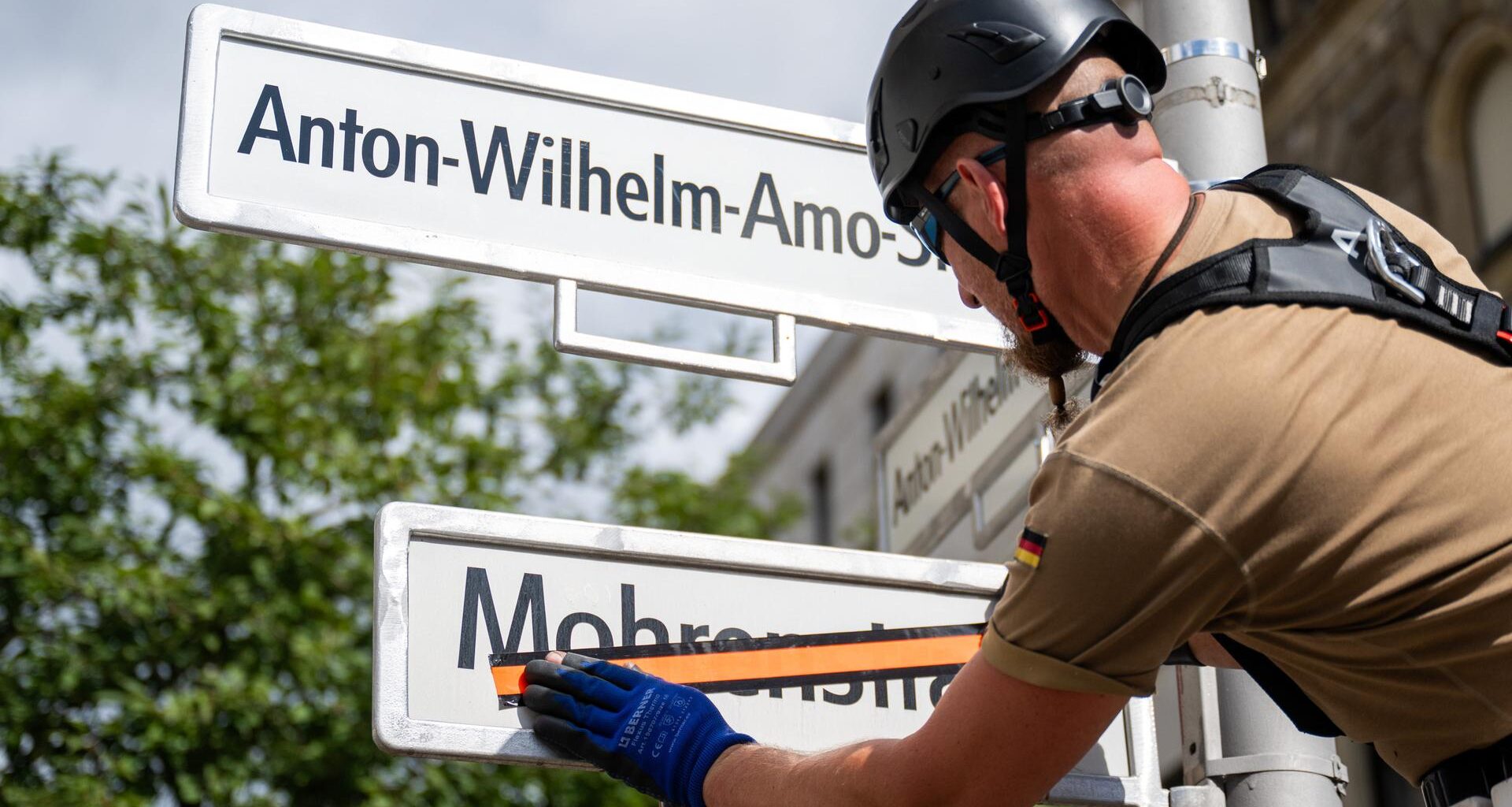 Ein Mitarbeiter einer Verkehrstechnikfirma überklebt ein Straßenschild mit der Aufschrift "Mohrenstraße". Darüber hängt ein neues Schild mit der Aufschrift "Anton-Wilhelm-Amo-Straße".