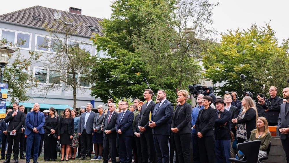 Politiker und Angehörige der Opfer stehen zusammen bei der Gedenkfeier ein Jahr nach dem Terroranschlag von Solingen.