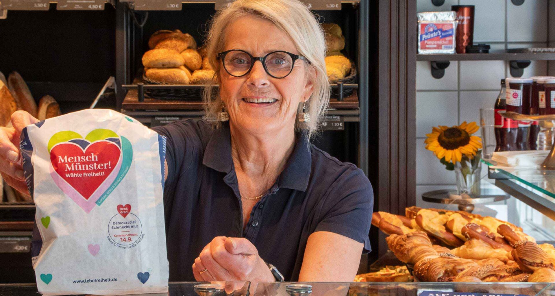 Verkäuferin hält eine Brötchentüte mit Aufdruck in einer Bäckerei