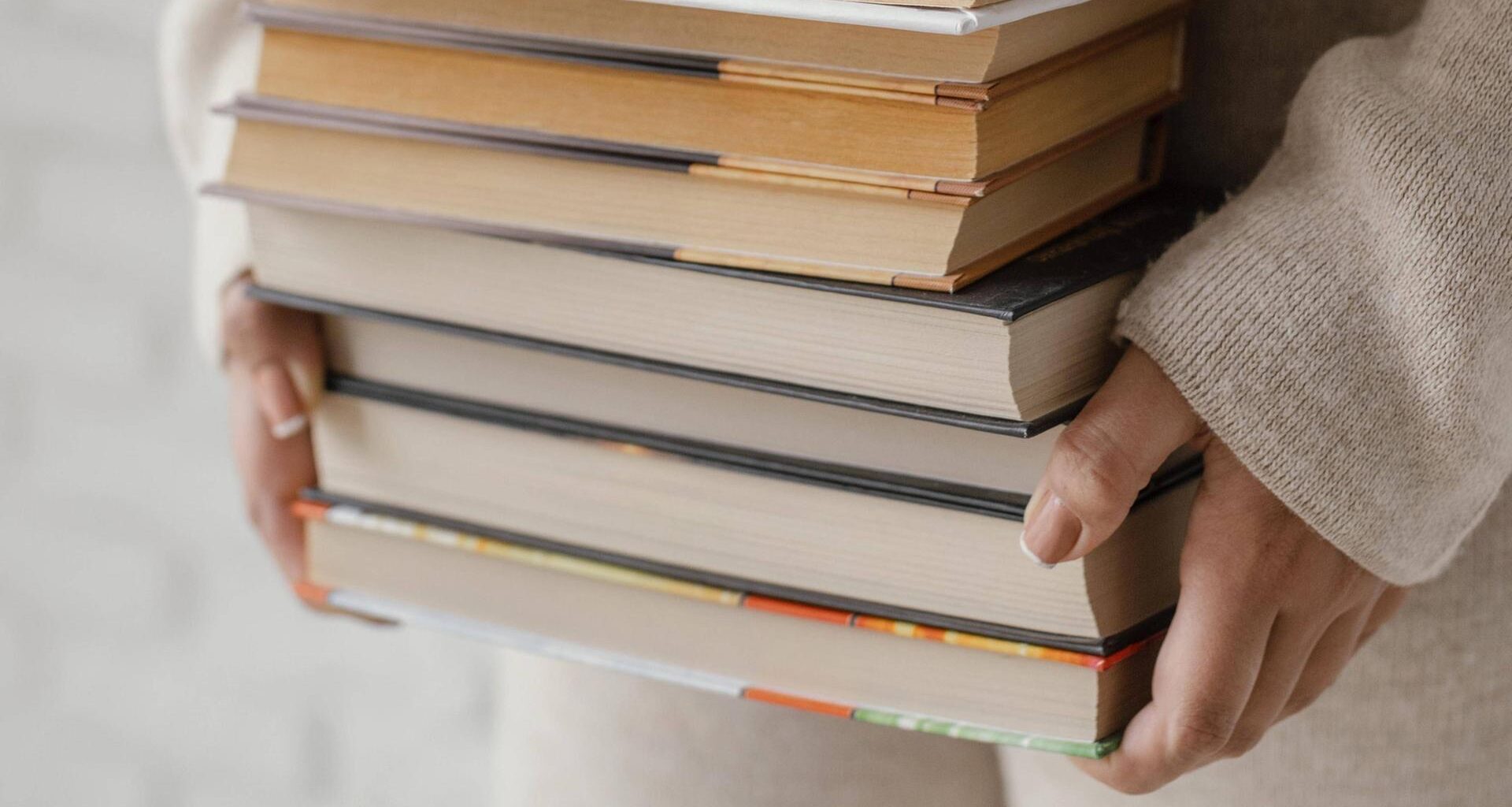 Frauenhände halten eine Stapel voller Bücher.