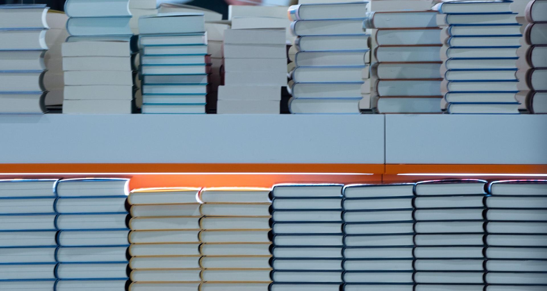 In einem Regal liegen Stapel von Büchern. Es ist ein Foto von einer Buchmesse.