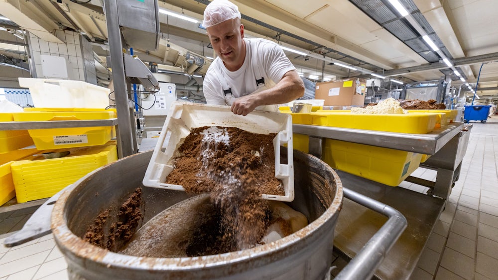 Ein Mitarbeiter des Lebkuchenherstellers Schmidt kippt in der Produktion verschiedene Rohstoffe zur Herstellung von Lebkuchenmasse in einen Behälter.