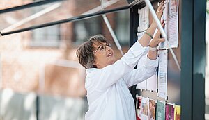 Sabine Schenzer befestigt in einem Schaukasten ein Plakat.