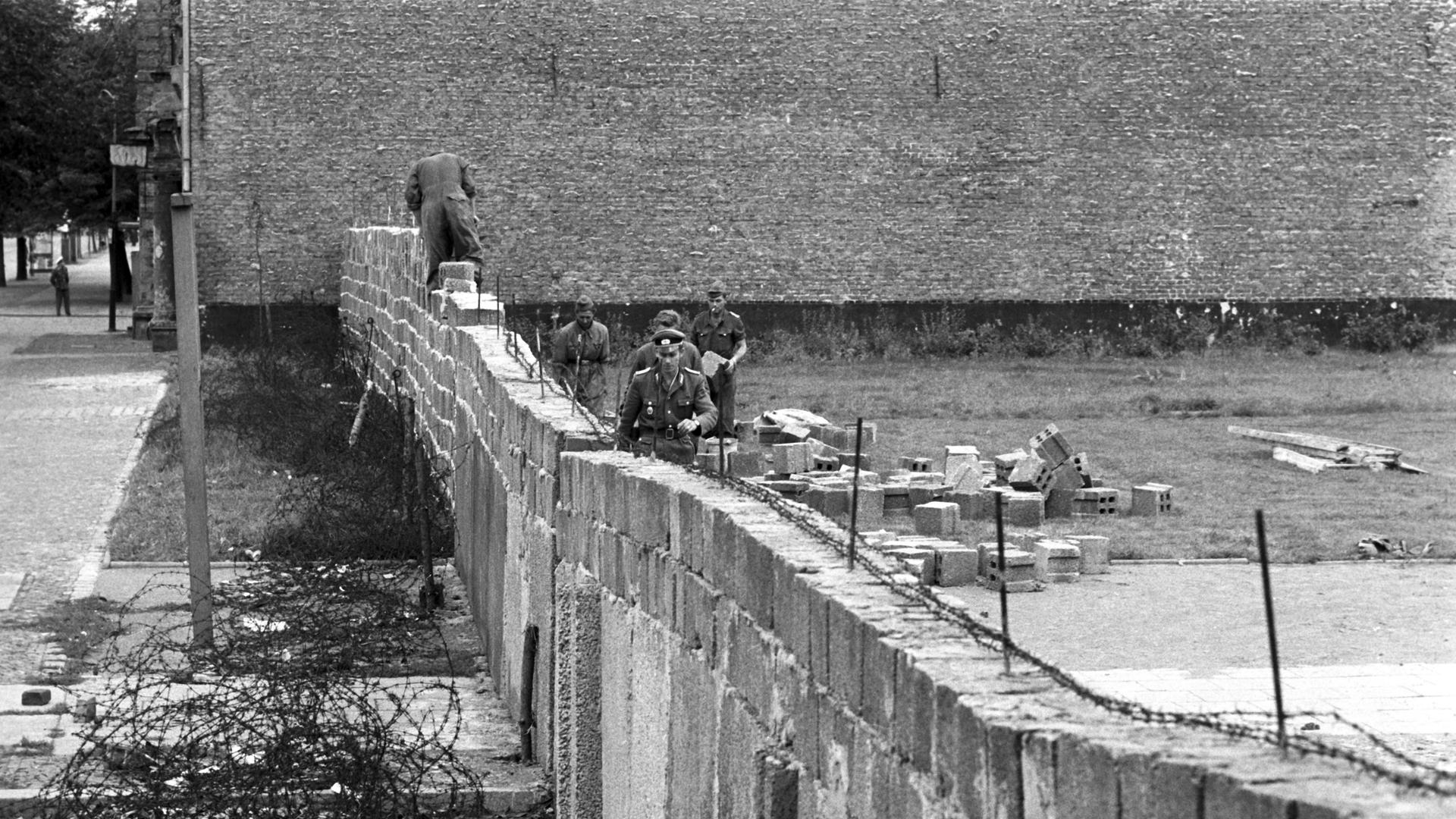 Volkspolizisten und Arbeiter der DDR beim Errichten der Berliner Mauer im Norden Berlins, an der Grenze zum westberliner Bezirk Reinickendorf. 