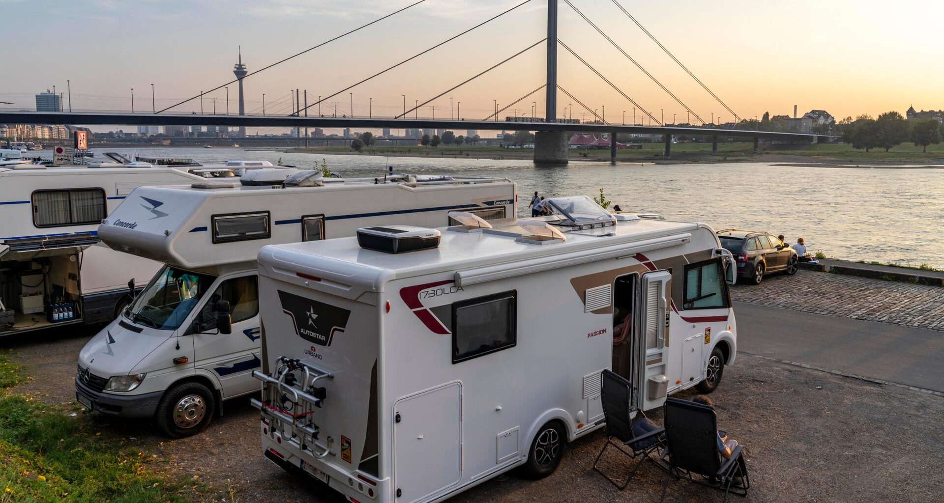 Ein Wohnmobil-Stellplatz am Rheinuferr in Düsseldorf, im Hintergrund eine Brücke