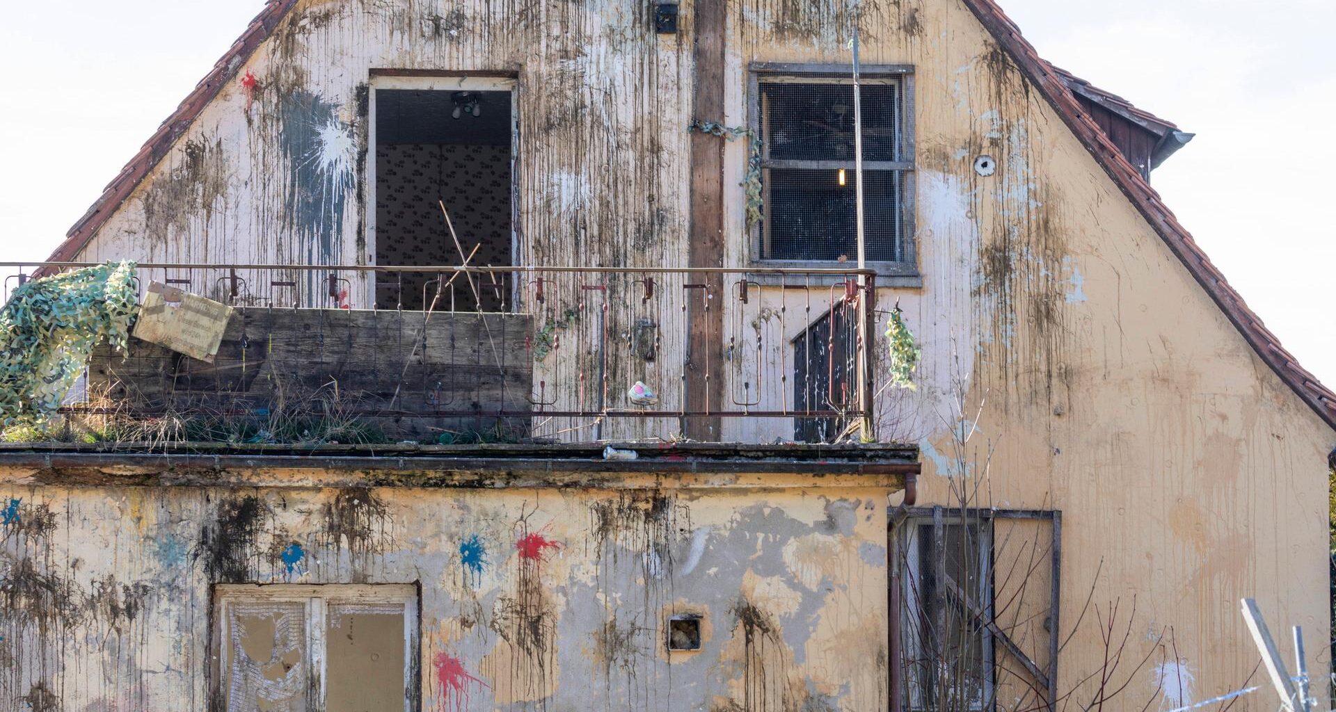 Frontalansicht der Fassade eines Hauses im desolaten Zustan, das mit zahlreichen Farbbeutel beworfen wurde.