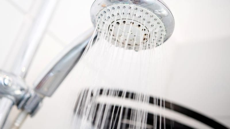 Ein Duschkopf hängt in einer Dusche in einem Badezimmer. (Symbolbild)