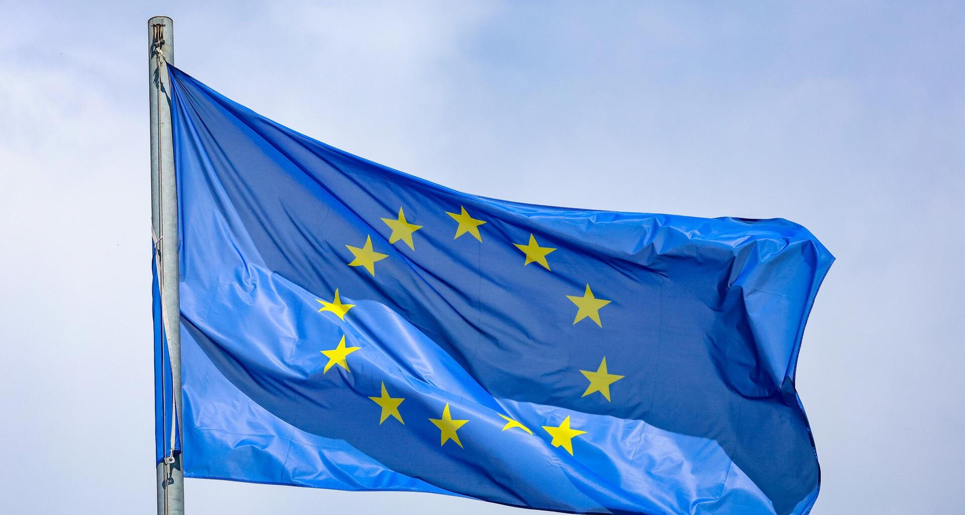 Eine EU-Flagge, die 12 Sterne auf blauem Grund zeigt, weht an einem Fahnenmast im Wind.