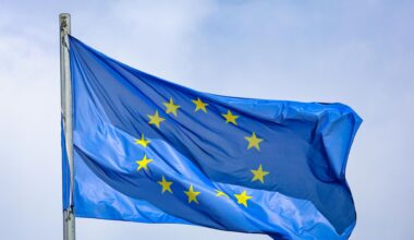 Eine EU-Flagge, die 12 Sterne auf blauem Grund zeigt, weht an einem Fahnenmast im Wind.