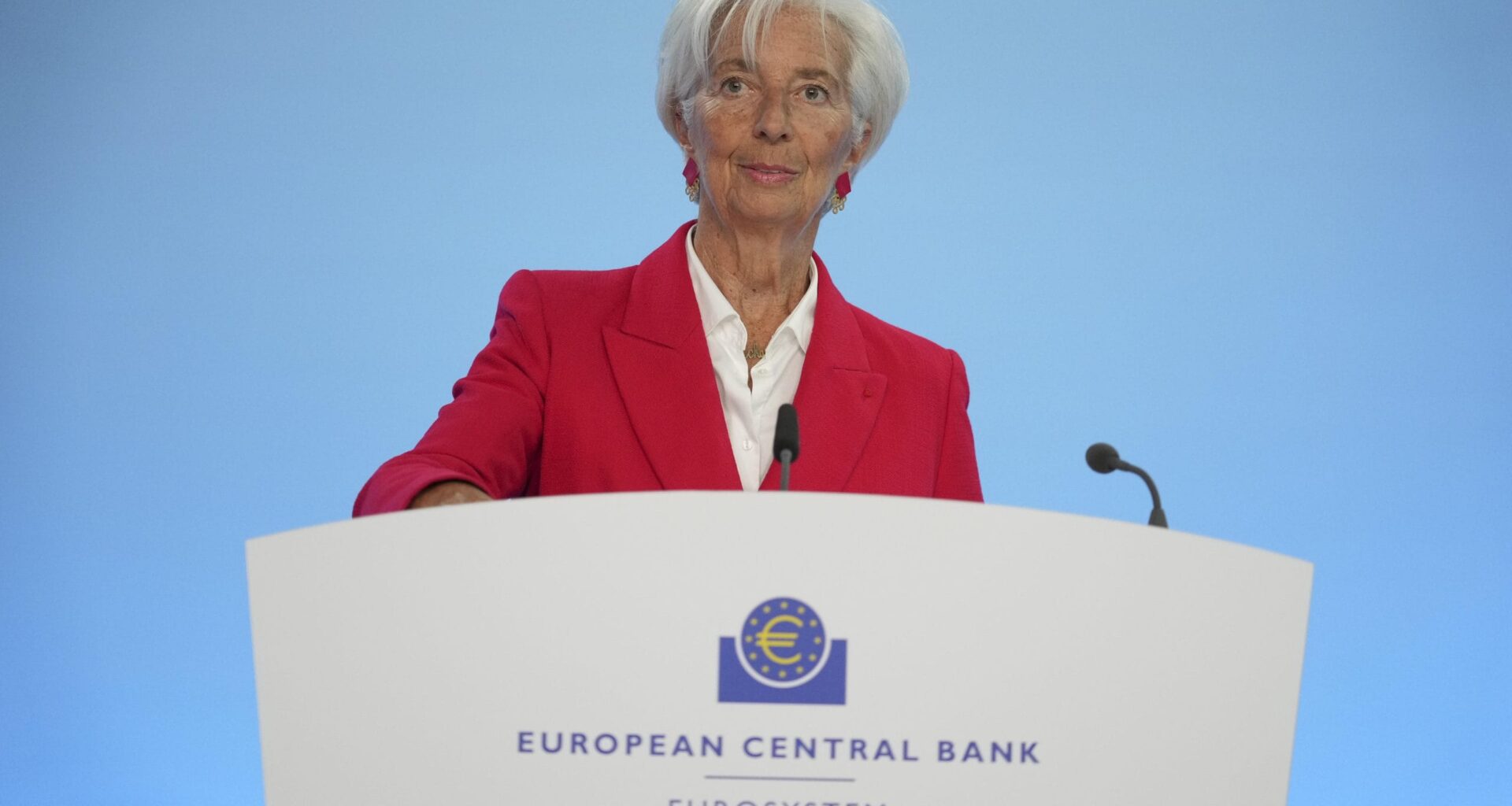 Eine Frau in einem roten Blazer steht an einem Podium mit der Aufschrift EZB Europäische Zentralbank Eurosystem und spricht vor einem blauen Hintergrund.