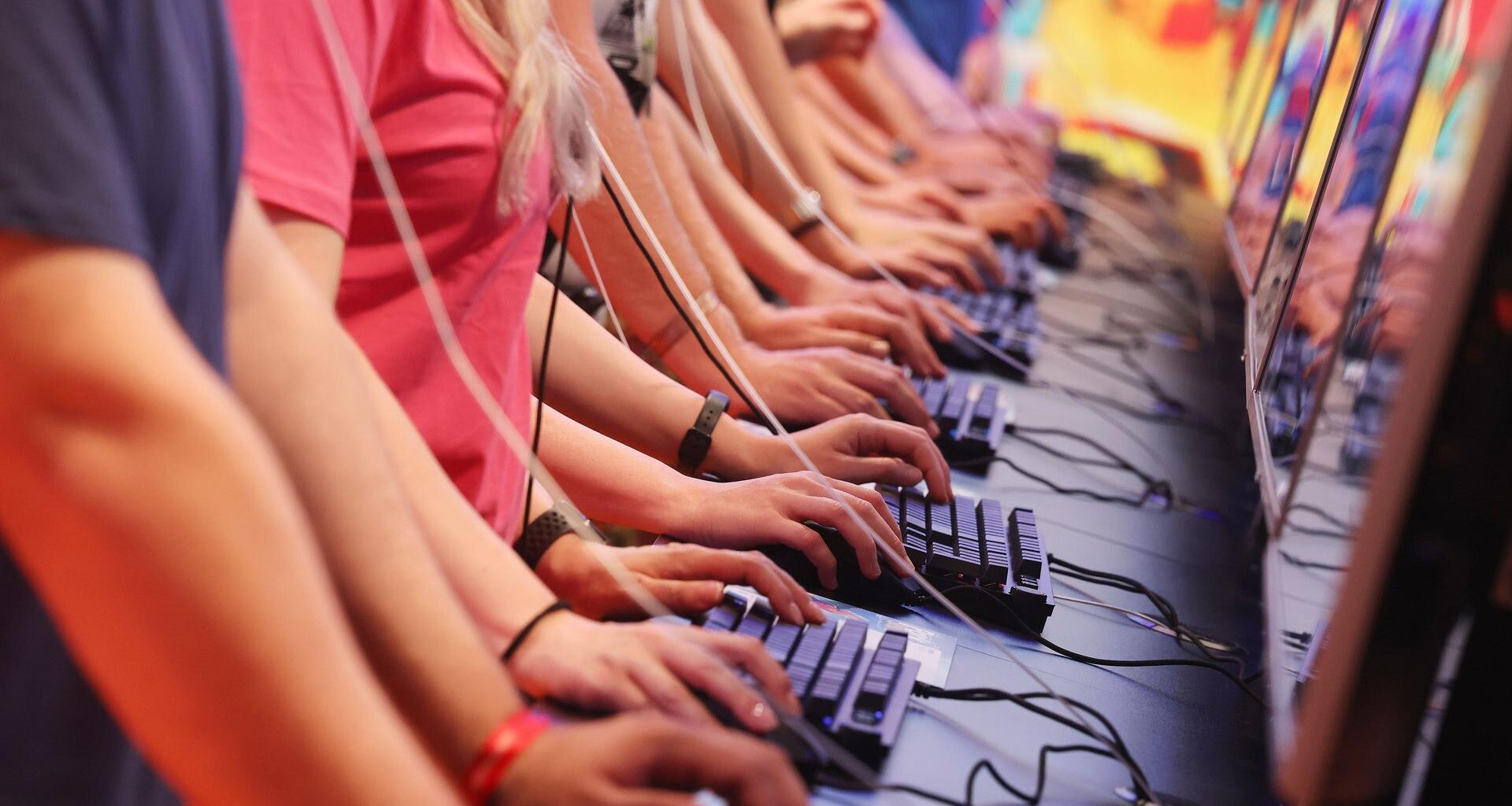 Junge Menschen stehen nebeneinander an Computertastaturen und spielen Videospiele.