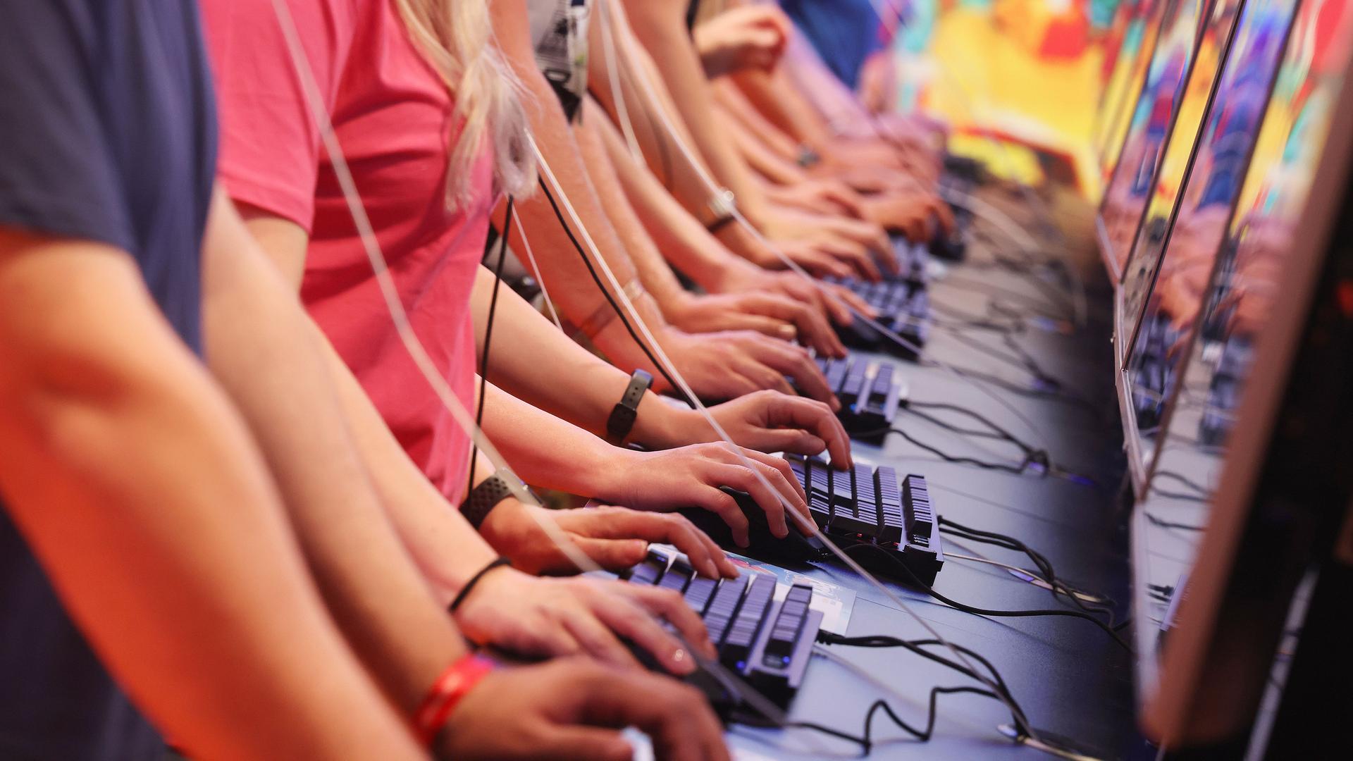 Junge Menschen stehen nebeneinander an Computertastaturen und spielen Videospiele.