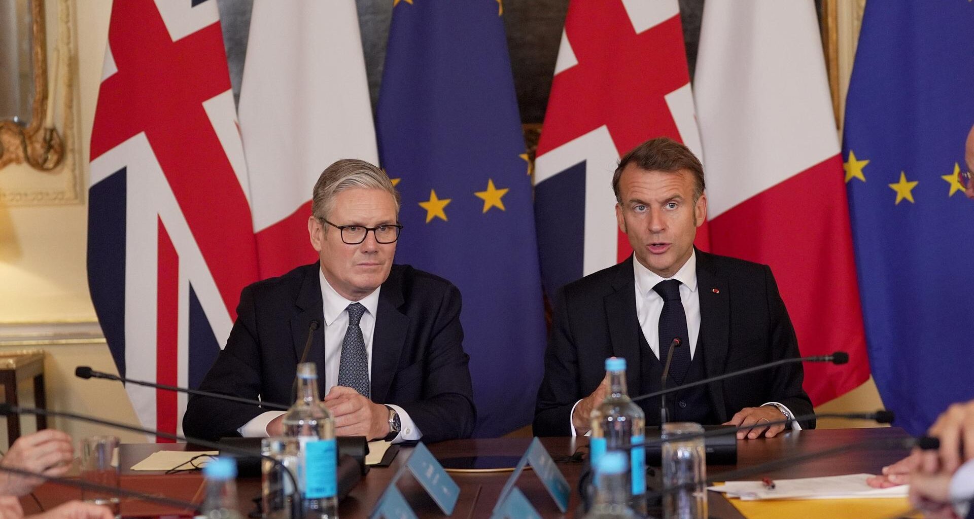 Der britische Premierminister Starmer und Frankreichs Präsident Macron sitzen nebeneinander, hinter ihnen die Landes- und die EU-Flagge.