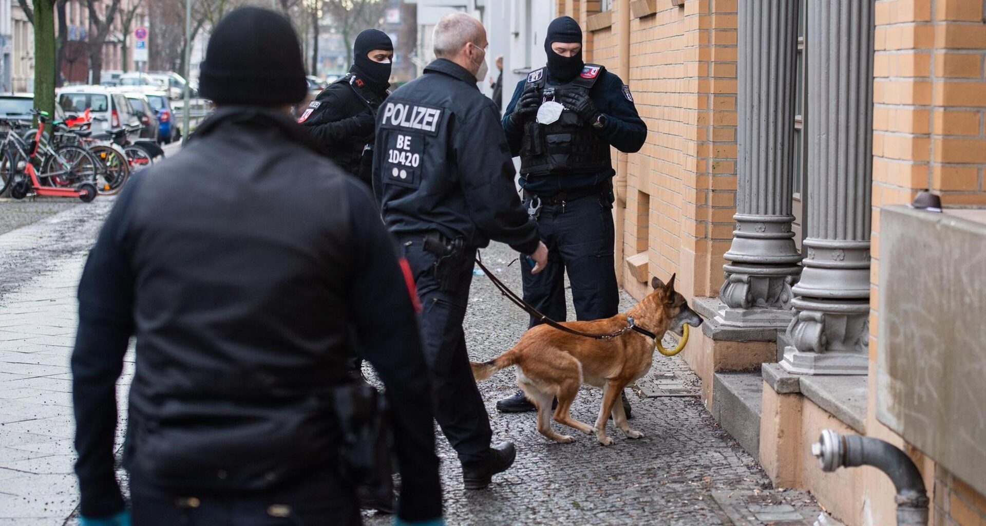 Berlin: Polizisten gehen bei einer Razzia mit einem Hund in ein Haus.