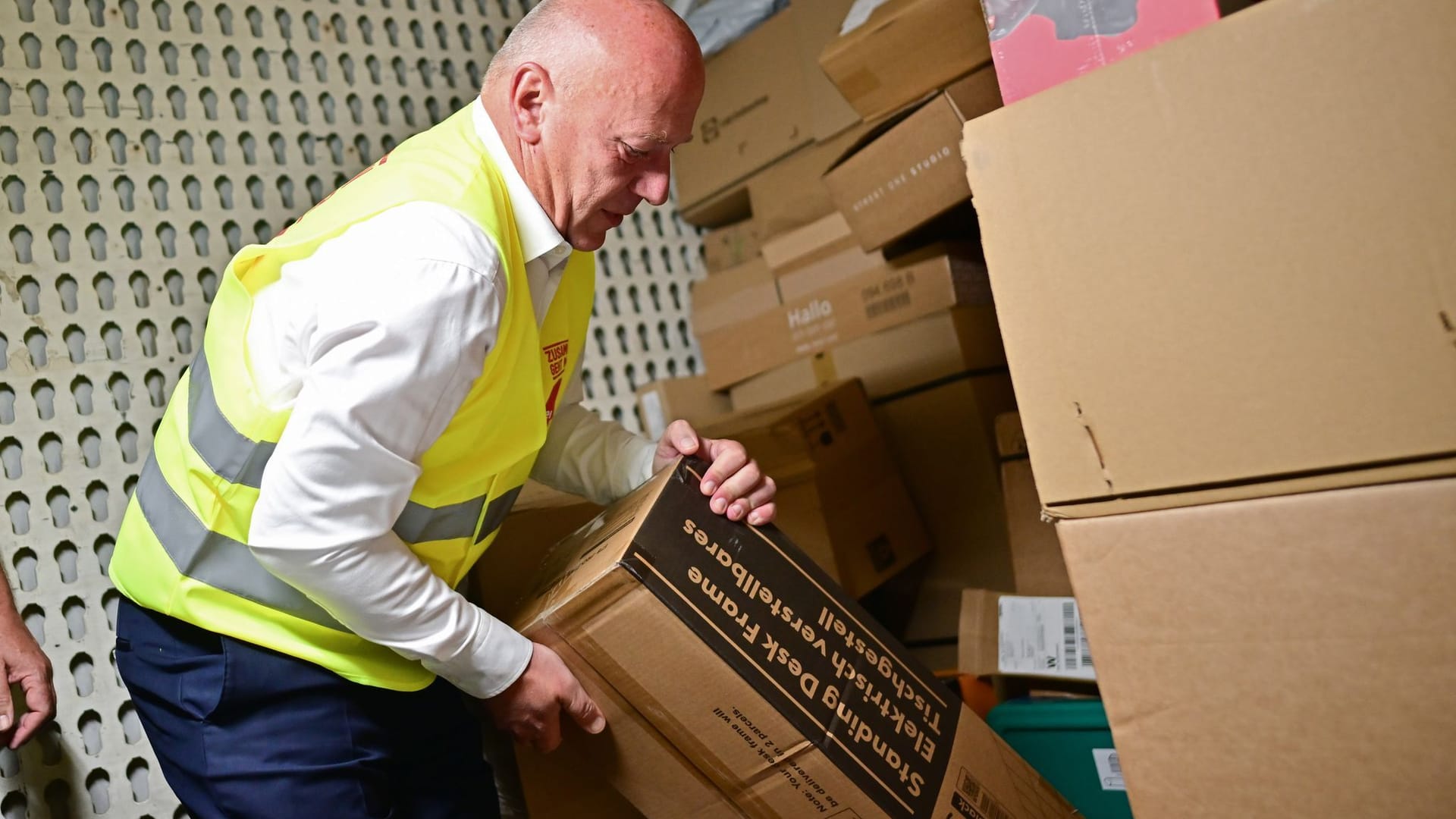 Kai Wegner (CDU), Regierender Bürgermeister von Berlin, nimmt während eines Besuchs in der DHL-Zustellbasis Charlottenburg ein schweres Paket aus einem LKW.