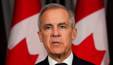 Der kanadische Premierminister Mark Carney steht im dunklen Anzug vor kanadischen Fahnen.