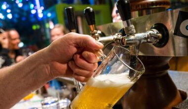 Nahaufnahme: In einer Bar zapft eine Hand Bier in eine Glas. Im HIntergrund unscharf Gäste.